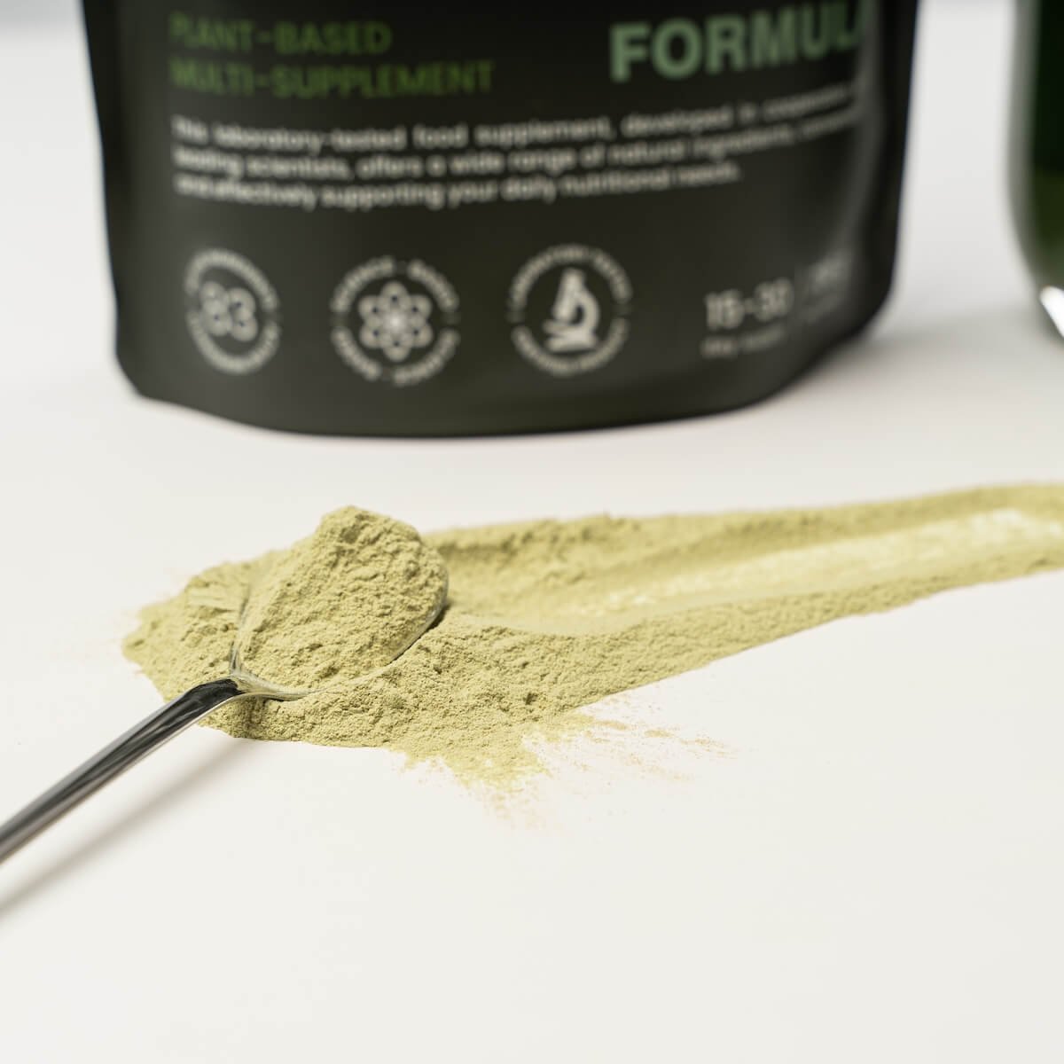 Greenish-brown True Habit powder on a silver spoon, with the product pouch in the background.