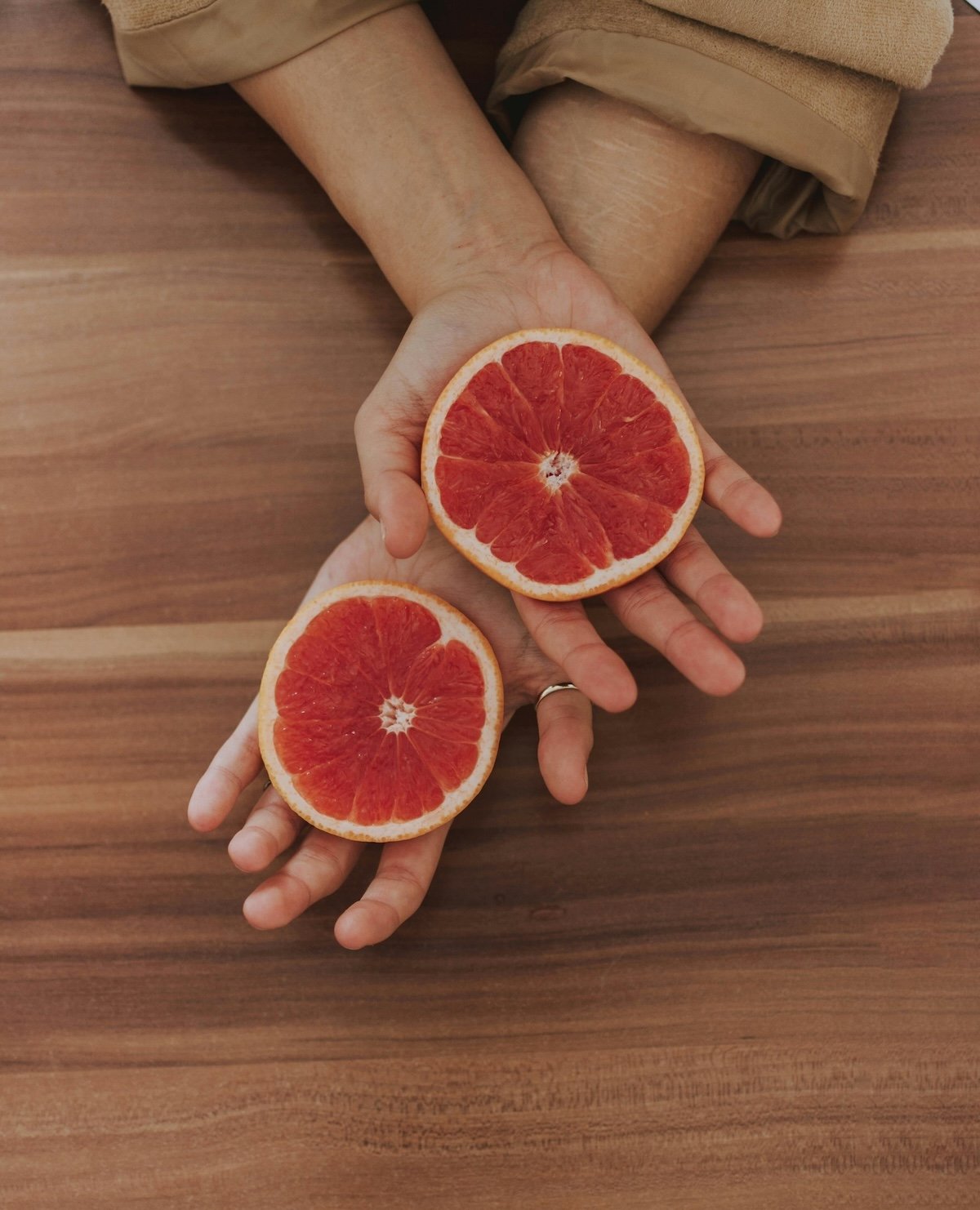 Hands holding two grapefruit halves, representing the individual ingredients and perfect balance of True Habit supplement.